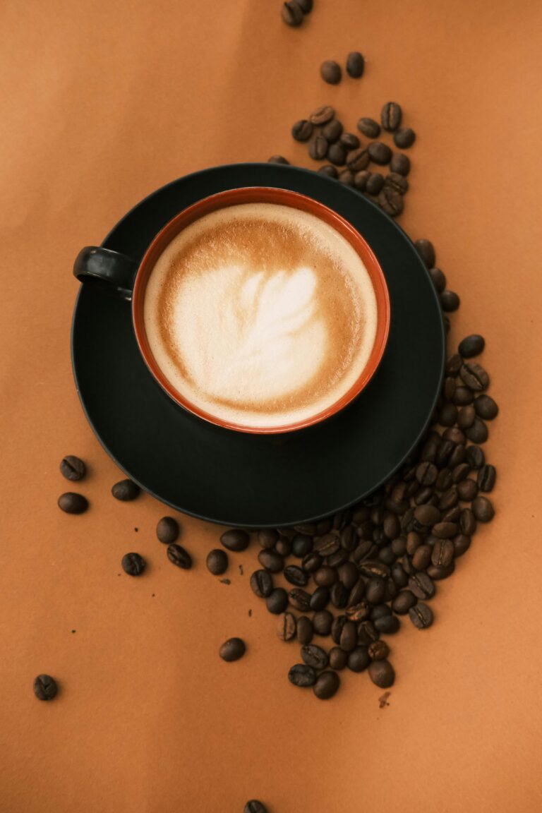 A beautifully crafted latte with coffee art surrounded by coffee beans on a rich brown background.